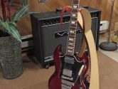 wood guitar stand holding a red Gibson SG, next an amplifier and house plant