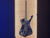 black autographed guitar in a lit display case, hanging on a blue wall