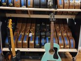 Fender and Guild guitars placed in front of a two tiered guitar shelf rack holding brown and black acoustic guitar cases