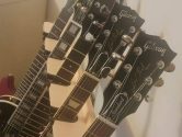 headstocks of 5 gibson guitars sticking out of the top of a wood guitar stand