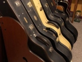 5 acoustic guitar cases in a wood rack