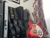 wood stand holding a rickenbacker guitar, on a wooden floor, next to guitar cases leaning against a wall