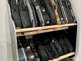 Bass guitar cases filling up a two-tiered shelf that rests on a hardwood floor