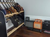 guitar shelf next to 4 amplifiers on a wood floor