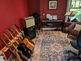 music room with multi guitar stand, amplifiers, keyboard, microphone and sheet music stand - all sitting on a worn out rug