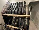 black acoustic and electric guitar cases filling a double decker guitar shelf in a white room next to a hallway
