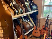 guitar cases on shelves, surrounded by individual guitar stands, on a stone tile floor, in a room with a bright window