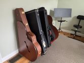 wood stand, holding acoustic and electric guitar cases, place against a wall,  next to a sheet music stand and stool