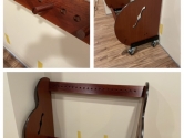 a cherry stained, empty, wood guitar case rack with pegs and wheels