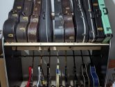 head-on view of a two tiered shelf system holding guitar cases on the top tier and guitars on the bottom.