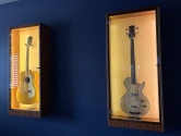acoustic and electric guitars in display cabinets hanging on a blue wall