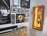 acoustic guitar in a wooden display case, next to a wall covered in music memorabilia