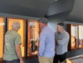 three men admiring autographed guitars in display cabinets