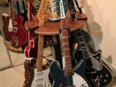 circular guitar stand holding a green rickenbacker and other assorted electric  instrumnets