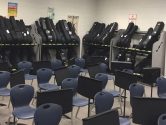 classroom with blue chairs and sheet music stands, and walls lined with guitar storage racks