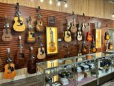 retail store with display case in front of a wall with hanging guitars and a lit cabinet