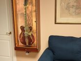 display case, hanging on a wall, holding eastwood 12 string guitar