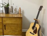 epiphone acoustic guitar in a wood stand next to a cabinet