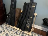 wood rack, on a carpet, holding cases for guitars, a banjo and more