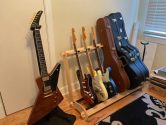 Wood guitar stand with 3 electric guitars and 3 cases, place in the corner of a room, next to a single guitar stand holding a Gibson Explorer