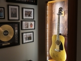 LED guitar display case with autographed Martin guitar, next to a memorabilia wall