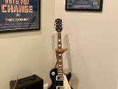 Epiphone Les Paul in a wood guitar stand, next to an amplifier
