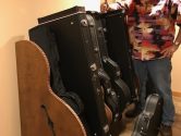 man smiling next to his collection of guitar cases