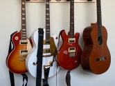 wall mounted hanger holding four guitars on a white wall