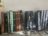 many guitar cases, placed against a wall, sitting on wood racks, and under a Telecaster hanging from the wall