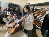 teacher showing a student how to hold an acoustic guitar in a classroom setting