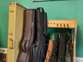 wood stand holding cases for ukuleles, mandolins and guitars, below a Rolling Stones poster