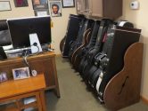 two walnut colored guitar case racks in an office next to a desk with a computer monitor