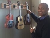 man pointing to his ukeleles hanging on the wall
