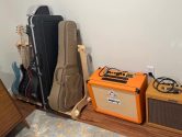 wooden rack holding 3 guitars and 3 cases, placed next to two amplifiers