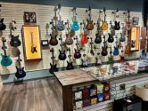 counter holding guitar strings, in front of a wall filled with guitars