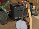 banjo resting in a wood guitar stand, in a recording studio, next to an amp and houseplant