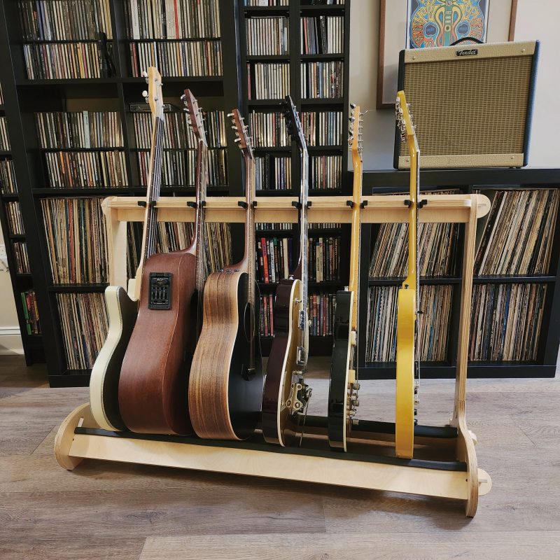 wooden 6 guitar stand in front shelves with albums, CDs and amplifier