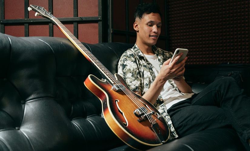 Person using smartphone, sitting on a couch, next to a semi-hollow electric guitar.